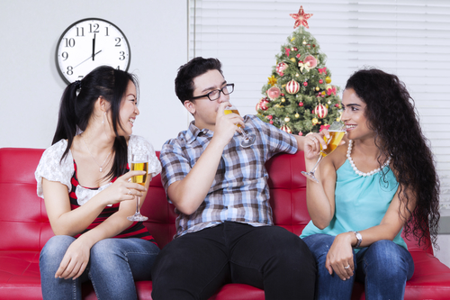 Portrait Of Three Happy People Sitting On Sofa While Drinking Champagne Together At Christmas Celebration